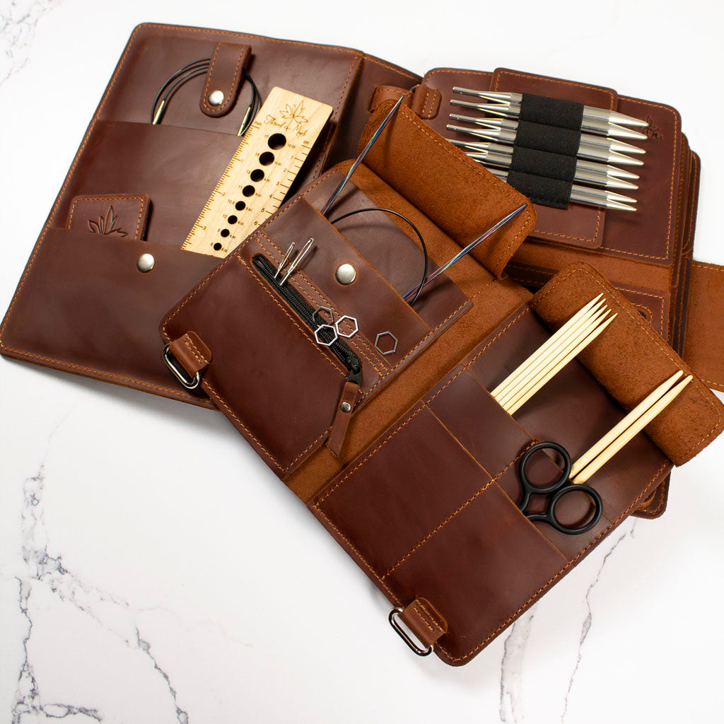 Brown leather knitting needle organizer with various knitting tools and accessories displayed.