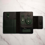 Open black and green leather tool organizer on white marble surface with pockets and snap closures.