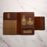 Brown leather travel organizer with multiple pockets and pen holder on a marble background.