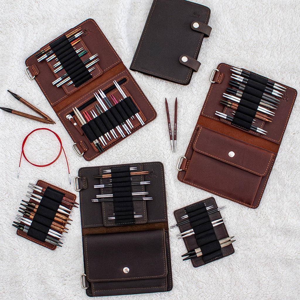 Assorted leather craft organizers containing knitting needles and accessories on a soft textured background.
