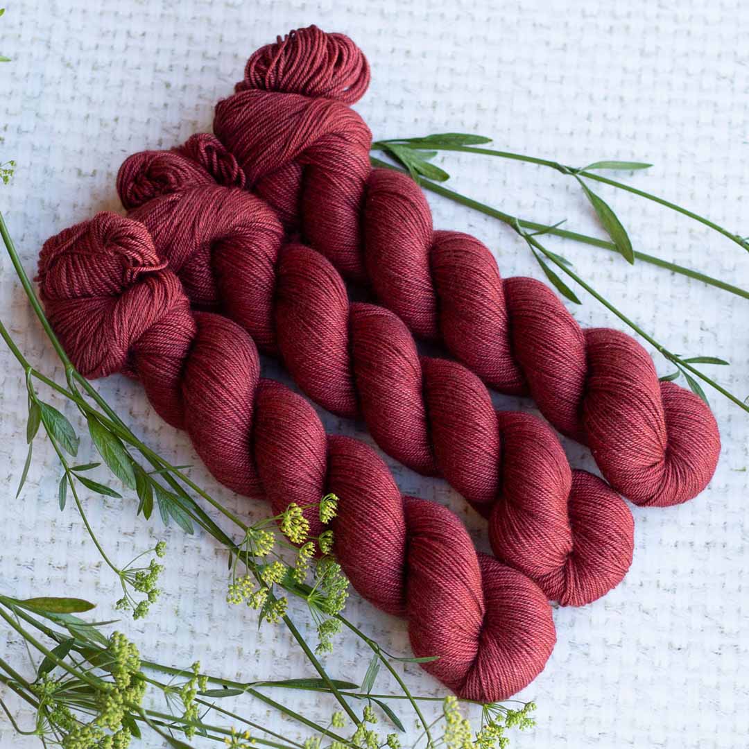 Red yarn skeins arranged with green leaves on a white textured surface.