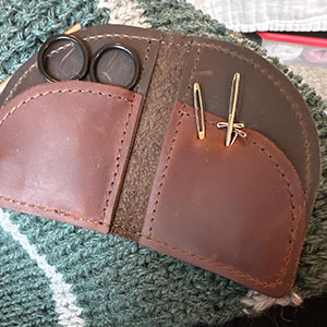 Leather sewing kit with scissors and needles on knitted fabric background.