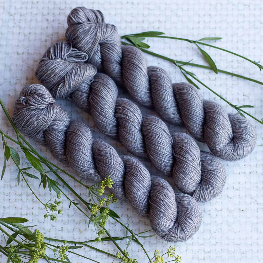 Three skeins of gray yarn arranged on a textured white surface with green floral accents.