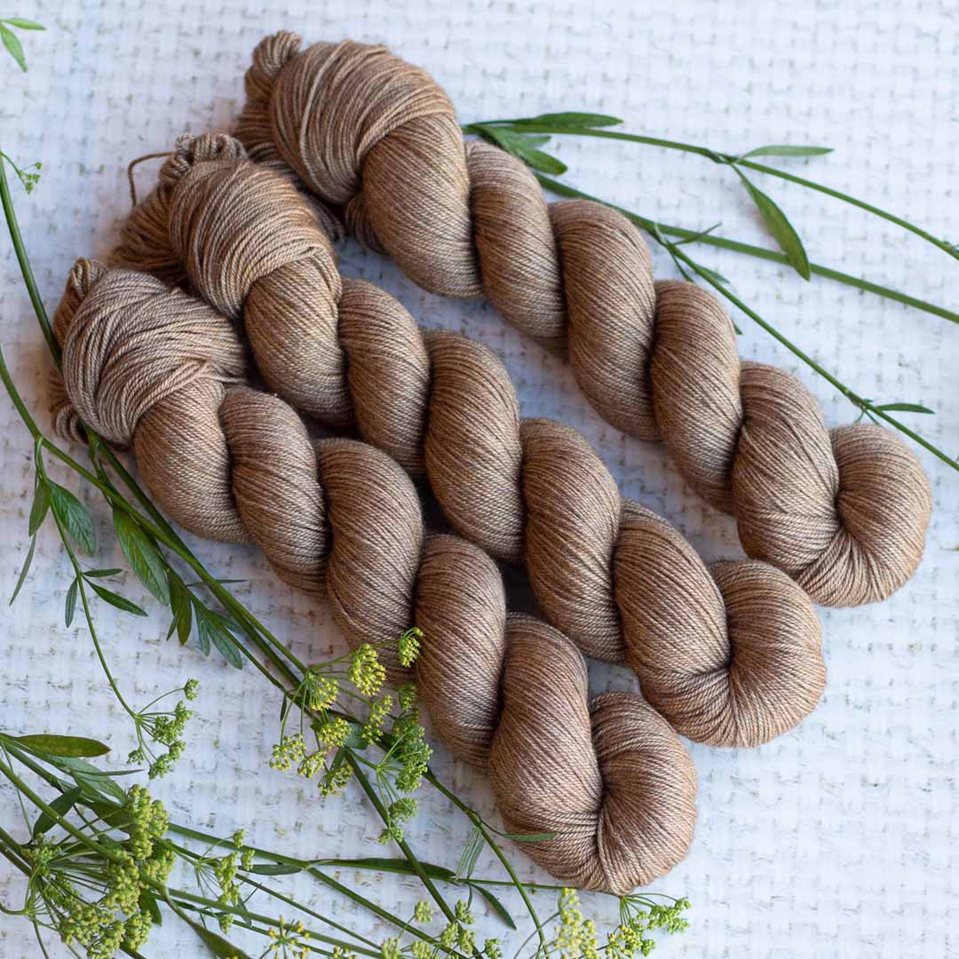 Three skeins of brown yarn with green plants on a textured white surface.