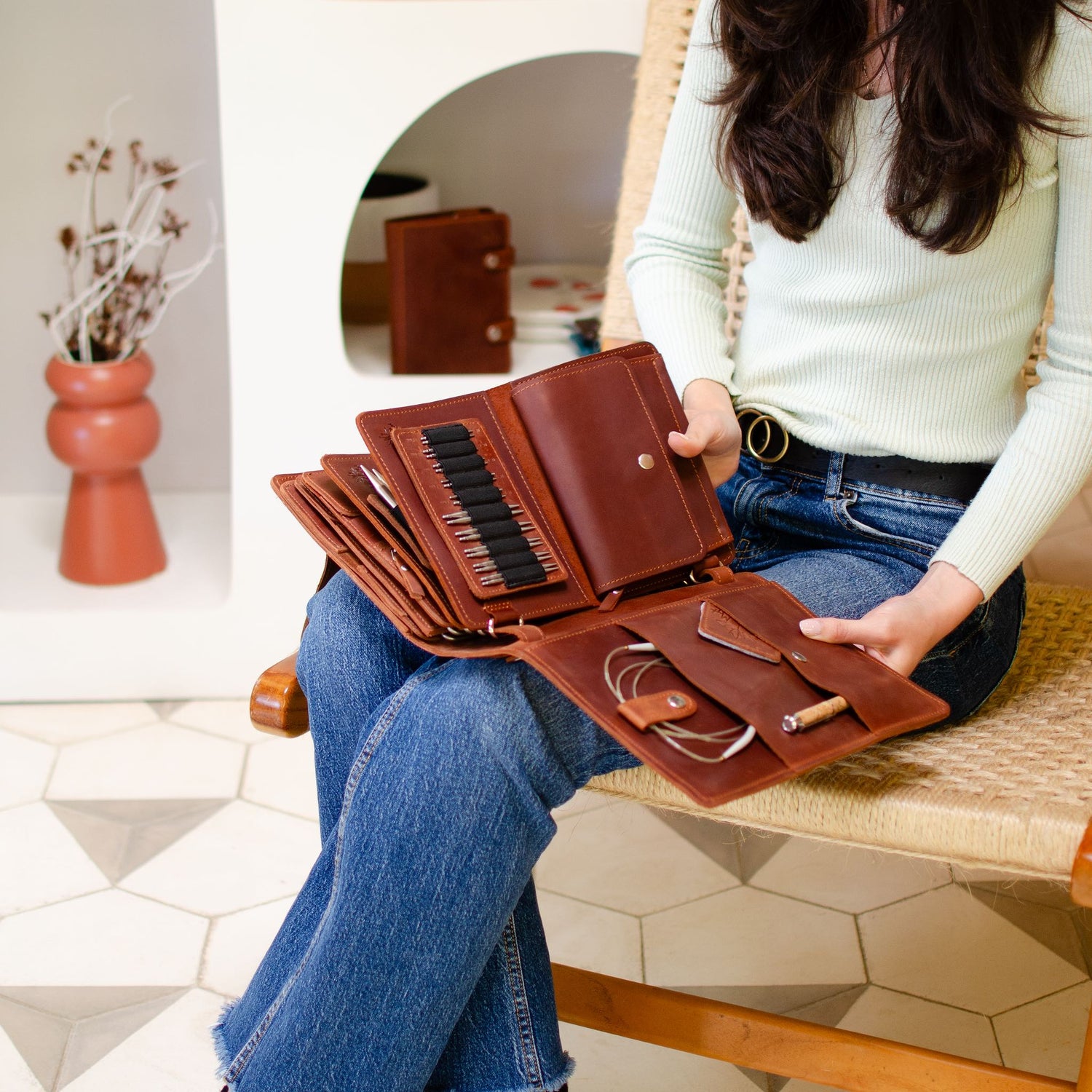 Woman sitting on a chair holding an open brown leather wallet with multiple compartments, displaying organization and craftsmanship.