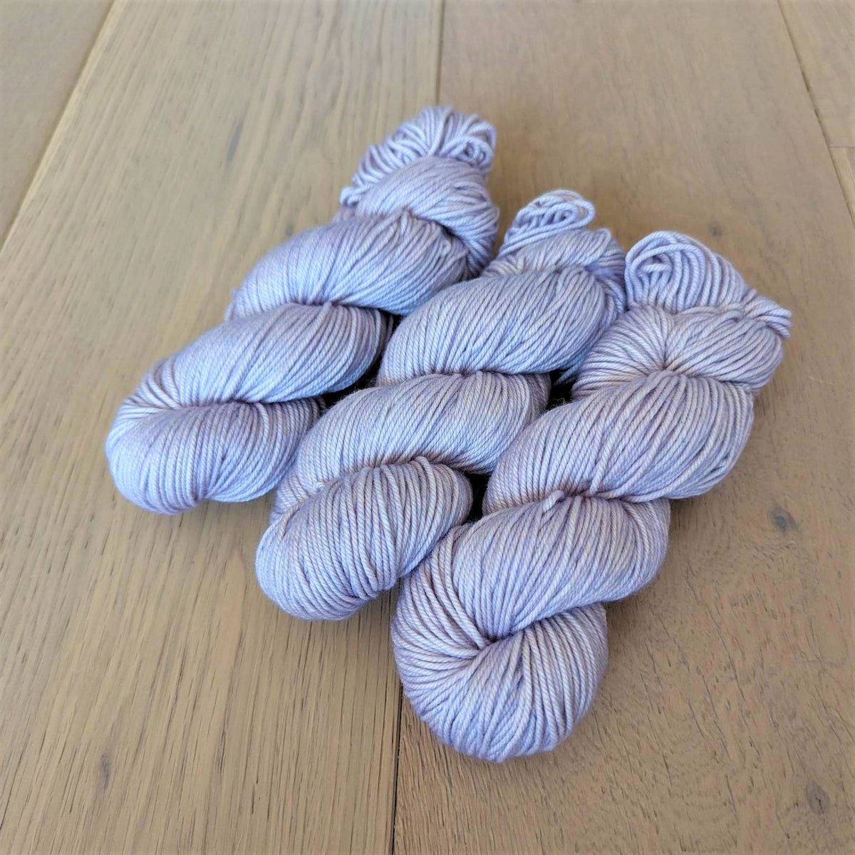 Four skeins of light purple yarn on a wooden surface.