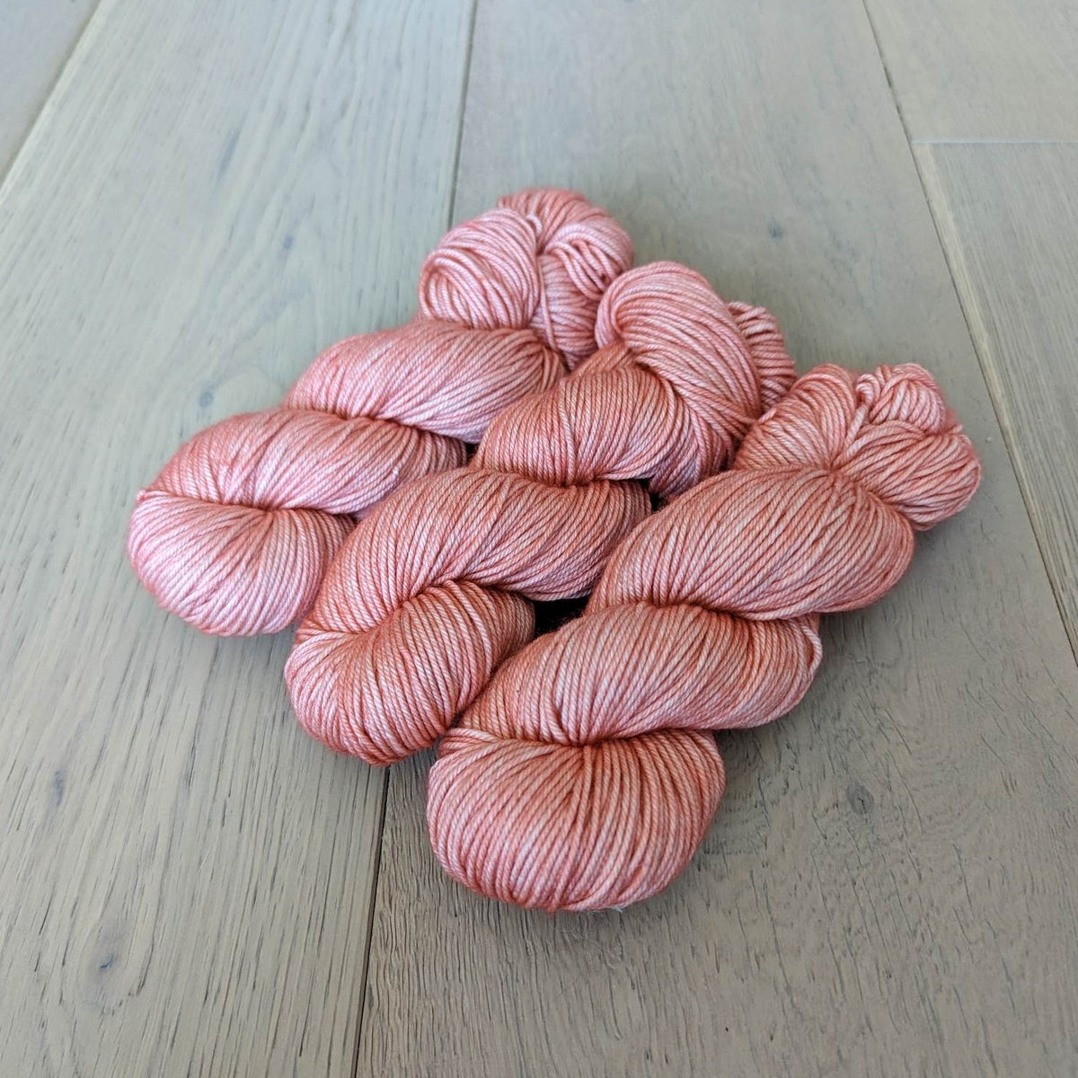 Five skeins of soft pink yarn on a wooden floor.