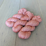 Five skeins of soft pink yarn on a wooden floor.