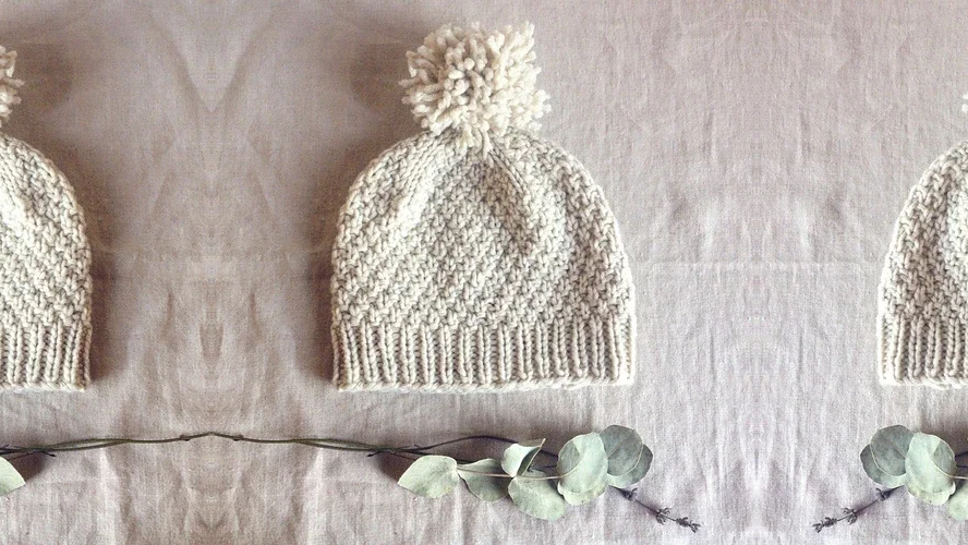 Cream knit pom-pom hat on linen. 