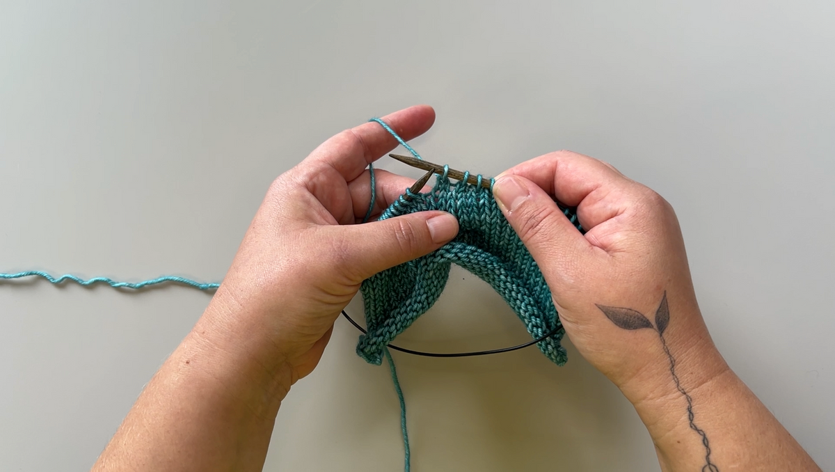 Two hands holding a piece of knitted fabric, demonstrating the knit 2 together decrease.