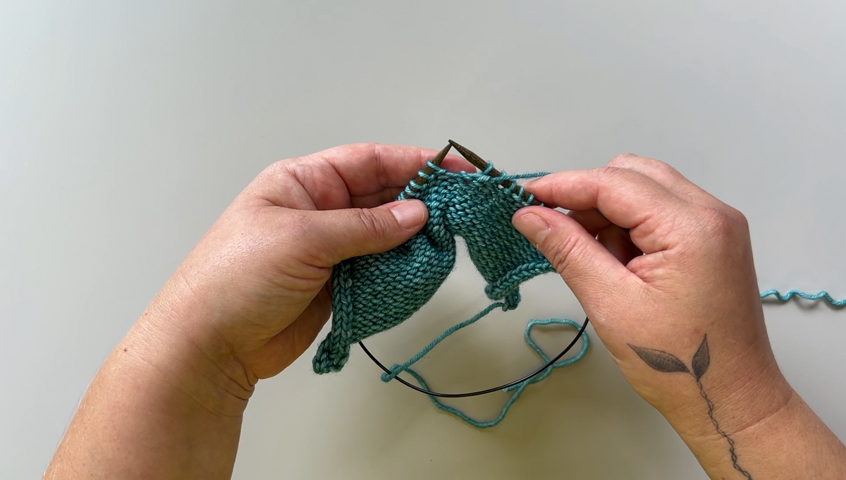 Two hands holding a small piece of knitted fabric, demonstrating the slip slip purl technique. 