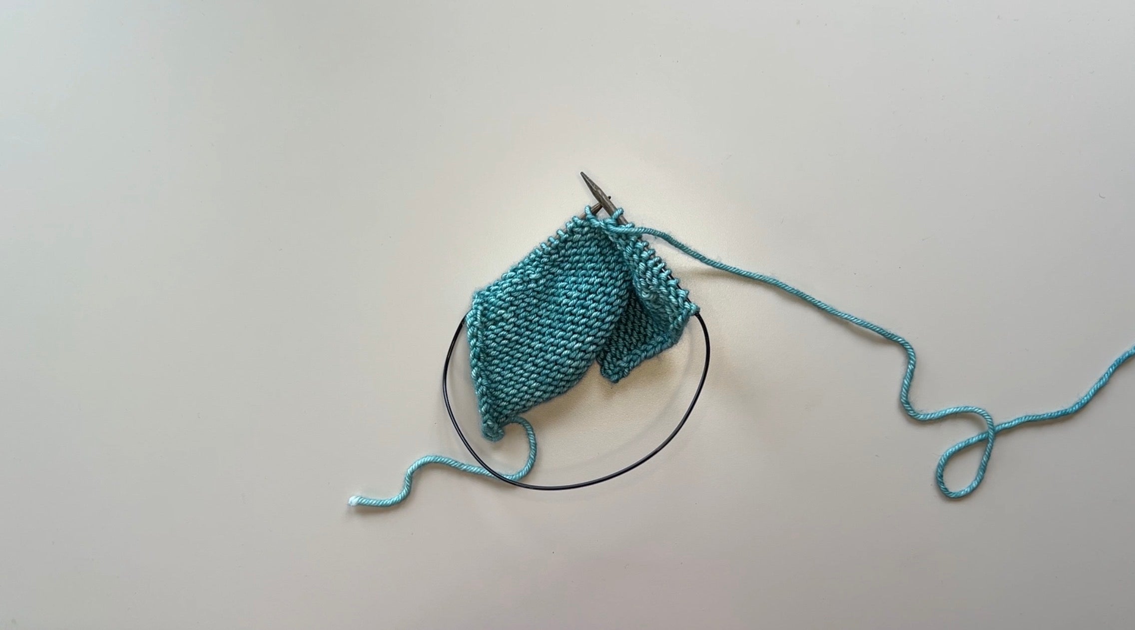 Teal knitted fabric on circular needles with the purl side showing.
