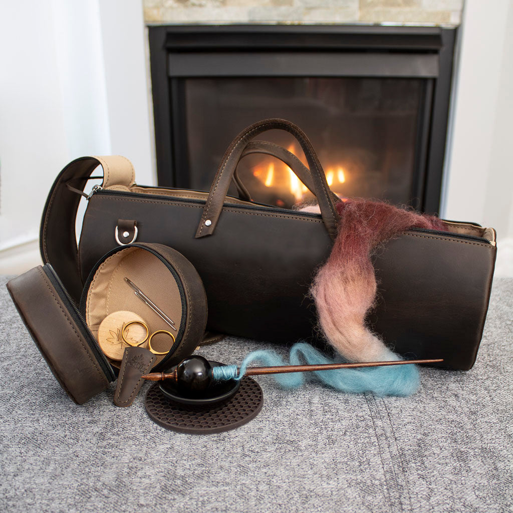 Leather knitting bag and spinning accessories with multicolored wool fiber in front of a fireplace.