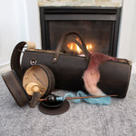 Leather knitting bag and spinning accessories with multicolored wool fiber in front of a fireplace.