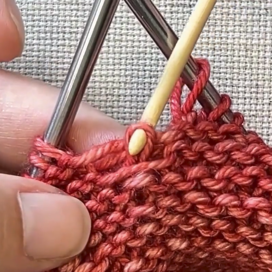 Close-up of knitting with red yarn and metal needles on a textured fabric background